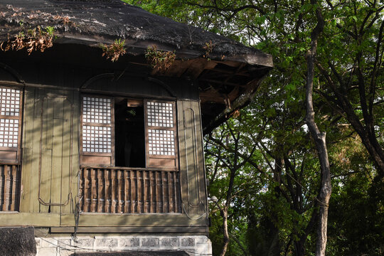 Traditional window and hut in the Philippines made of wood and shell. Roof made of straw. Trees surrounding an old house.