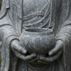 Fototapeta premium Stone Buddha statue hand gently cradling an alms bowl with rainwater collected inside
