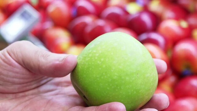 Close-up view of a hand holding a green ripe apple in a grocery store. A customer choosing organic healthy food in a supermarket.