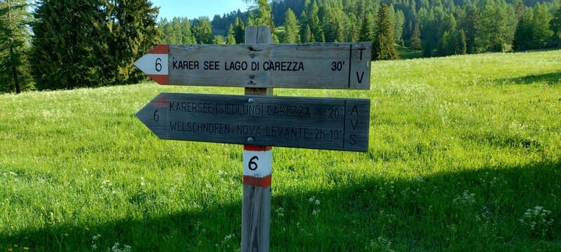 Cartello escursionistico in legno con segnavia verso il Lago di Carezza nelle Dolomiti