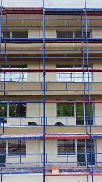 Workers are busy constructing a multi-storey building with scaffolding surrounding the structure. Windows are being installed as part of the building process.