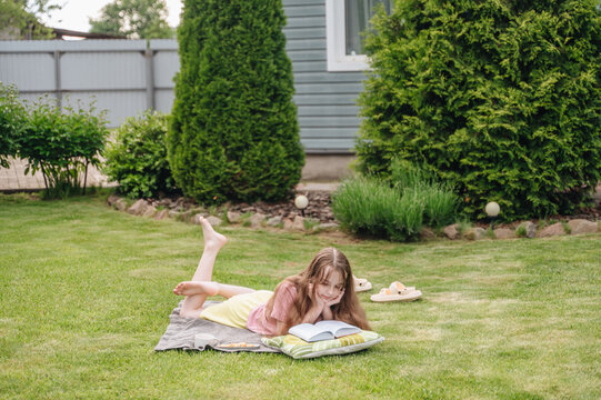 Child resting and reading book on green lawn