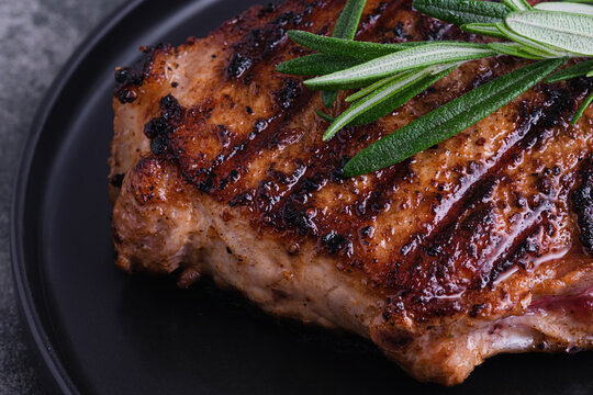 Close up a of grilled steak is placed on a dark plate. Fresh green herbs sit a top the meat. top view