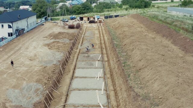 Wide aerial drone shot of long foundation trench with concrete footings and wooden formwork at active construction site of future residential building. Perfect for construction, real estate, and devel
