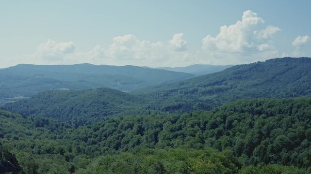 Wide cinematic aerial drone shot of scenic Carpathian mountain valley with rolling forested hills, small settlement visible below, and dramatic cumulus clouds above. Perfect for nature, travel, Ukrain
