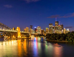 Obraz premium Illuminated Urban Skyline Glowing at Night Along River with Bridge