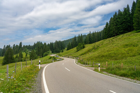 The Riedberg pass road in the Bavarian Alps on a cloudy summer day - green alpine meadows and trees can be seen on both sides