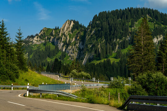 The Riedberg pass road in the Bavarian Alps in front of impressive rocky mountains on a sunny summer day with blue sky