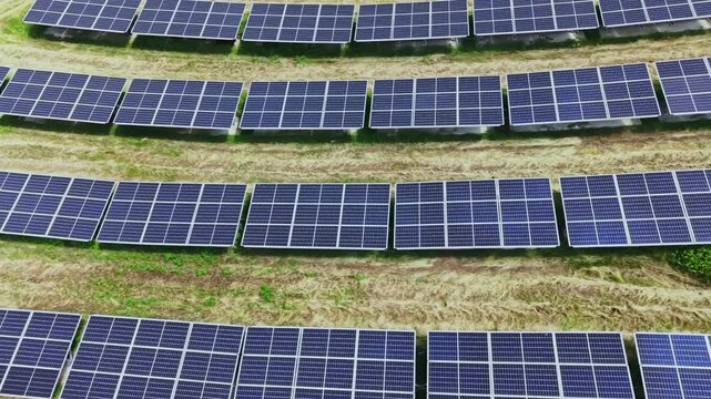 Aerial solar farm rows of panels, closeup drone view showing linear arrays on green grass, maintenance tracks and access corridors, reflective photovoltaic