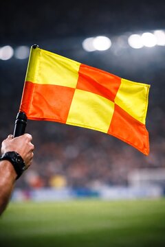 Macro sports shot of a yellow and orange offside flag waving during a tense football match, shallow depth of field.