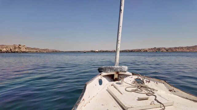 Point of view shot from the bow of a traditional motorboat sailing on the clear blue waters of the nile river towards philae temple in egypt