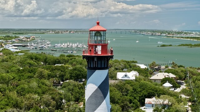 Aerial view of the St. Augustine Lighthouse on Anastasia Island with people on the gallery overlooking the Matanzas River and coastal greenery in St. Johns County, Florida, United States.