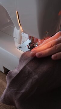 A tailor sews on a sewing machine. A straight stitch is laid across the linen fabric. Close up vertical scene with sewing machin. 