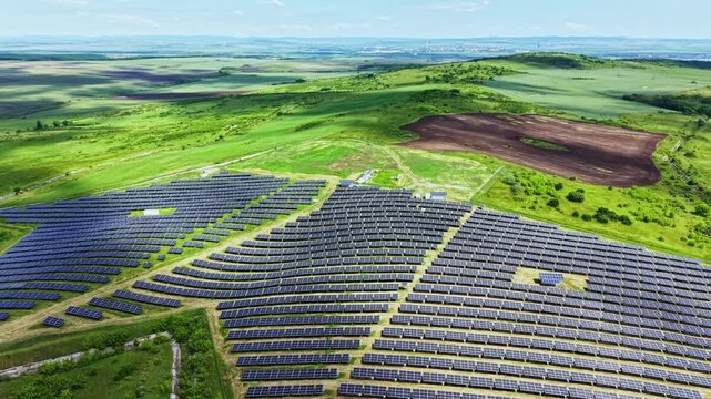Aerial hilltop solar array sweeping pattern across verdant hills, spiral layout with biodiversityfriendly groundcover between modules, panoramic horizon
