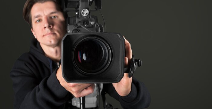 Male videographer operating professional video camera in studio on dark background