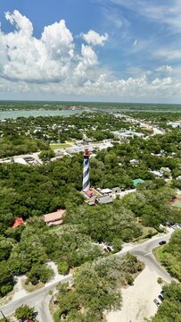 Aerial view of the St. Augustine Lighthouse with black and white spiral stripes surrounded by lush green trees on Anastasia Island in St. Johns County, Florida, United States.