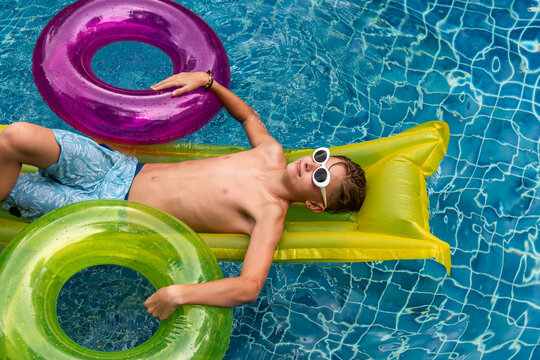 Young Caucasian boy relaxing on pool float with colorful inner tubes
