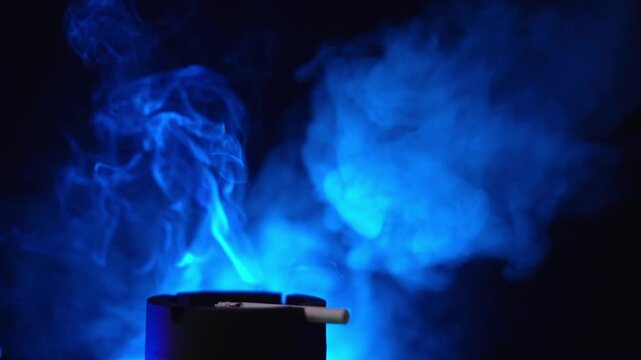 Close up 1080p 120fps slow motion video of burning cigarette smoke swirling under blue neon light in darkness