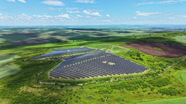 Aerial solar farm green countryside spiral array, expansive photovoltaic installation on rolling hills under clear sky, patchwork fields and access roads, drone