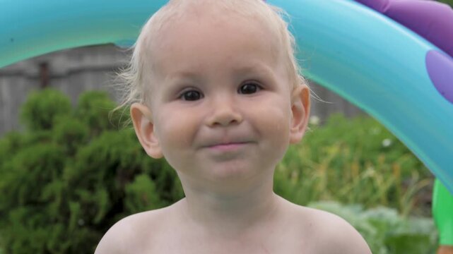 Close up of cute blond toddler boy in an inflatable pool outdoor. Baby showing a wide range of emotions from happy laughter to a serious and thoughtful expression in his backyard during summer