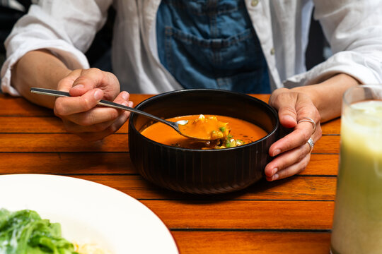 Person eating spice tomato soup from a black ceramic bowl