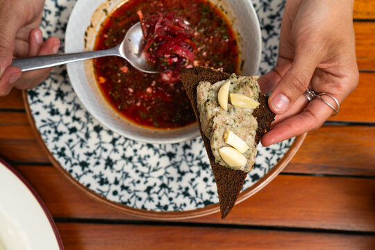 High angle view of a person holding dark rye bread with lard spread and garlic over borscht soup