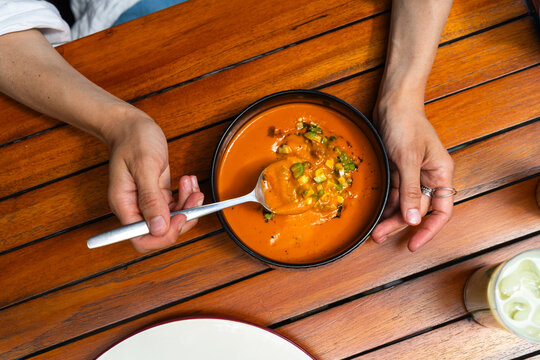 person eating refreshing tomato soup with a spoon from a black bowl