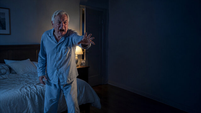 Frightened elderly man reaching out in dark bedroom at night