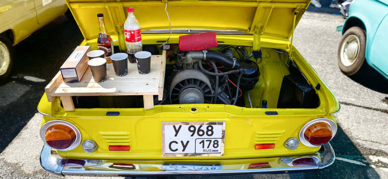 Saint Petersburg, Russia - May 23, 2026: Zaporozhets car with open hood displaying engine, wooden platform with drinks and cups on top, parked in a sunny outdoor setting