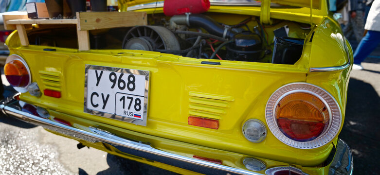 Saint Petersburg, Russia - May 23, 2026: Zaporozhets yellow vintage car with open trunk revealing engine and license plate, parked on a street with blurred background