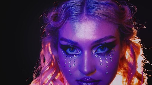 Portrait beauty face fashion model posing dancing blonde hair woman creative graphic make up shiny rhinestones glitter. blue pink purple neon light teen girl looking camera close-up eyes art make-up