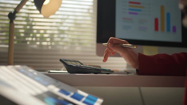 Close up of a business person's hand calculating finances in a modern office. An accountant analyzing charts and graphs on a computer