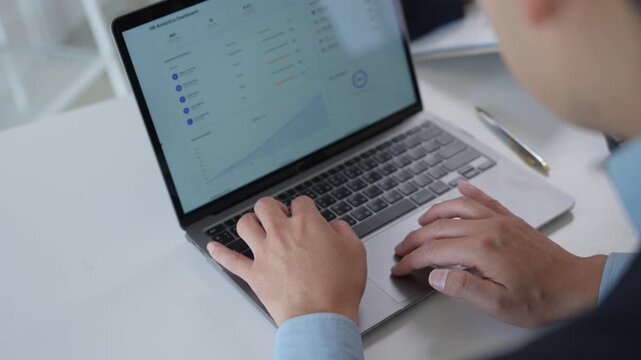 Businessman's hands typing on a laptop and using a trackpad to analyze human resources data, charts, and graphs on a dashboard