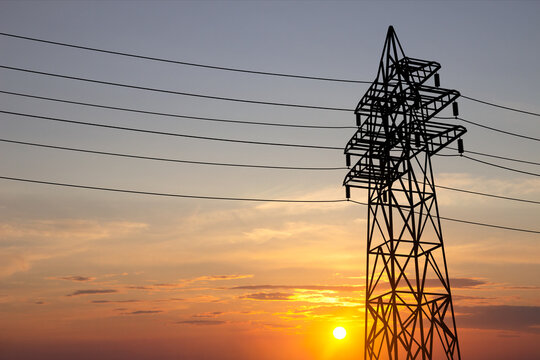 Silhouette of a metal transmission tower with power lines against the sunset