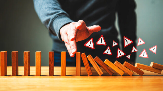 A person stops falling dominoes with warning signs from falling further on a table