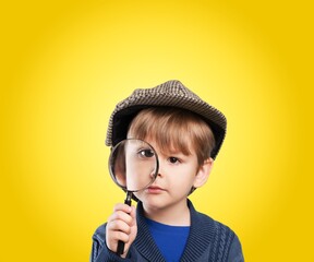 Little boy in flat cap looking through magnifying glass over yellow background © BillionPhotos.com