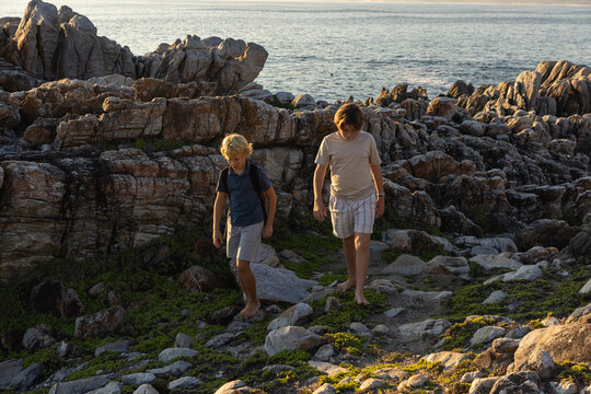 barefoot pre teen boys climbing and exploring rocky coastline of DeKelders, South Africa