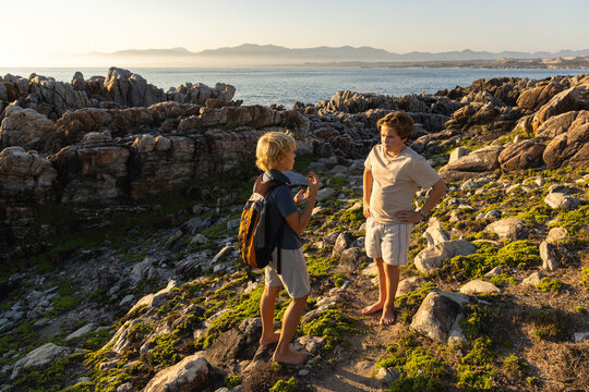 barefoot pre teen boys climbing and exploring rocky coastline of DeKelders, South Africa