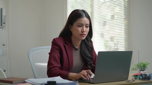 Overworked asian woman feeling stressed and tired from long hours working on a laptop in the office, suffering from a severe headache
