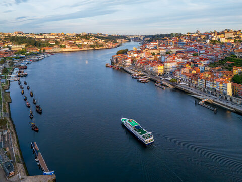 Drone view of Douro River in Porto, Portugal, with a tourist boat between Ribeira and Vila Nova de Gaia, with moored rabelo boats at sunrise