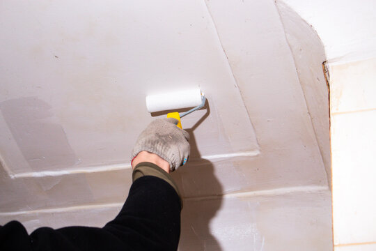 Man holding roller near freshly painted ceiling. Enjoyable weekend project. Cosmetic renovation done simply and affordably