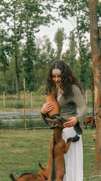 Young woman in traditional clothing interacting with goats on a farm
