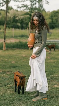 Young woman in traditional attire holding a clay pot with a goat nearby