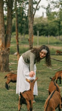 Young woman interacting with goats in a pastoral setting during daytime