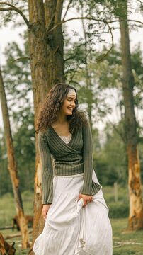 Young woman with curly hair wearing a green sweater and white skirt in a forest