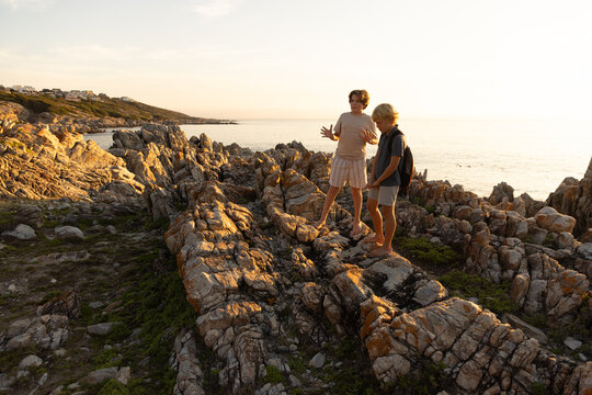 2 pre teen boys climbing and exploring rocky coastline of DeKelders, South Africa