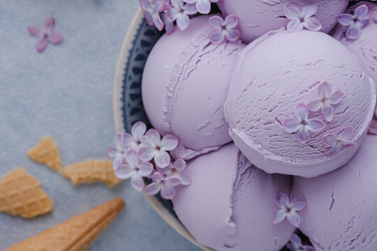 Close up of creamy lavender ice cream scoops topped with delicate lilac blossoms. Healthy frozen dessert. top view