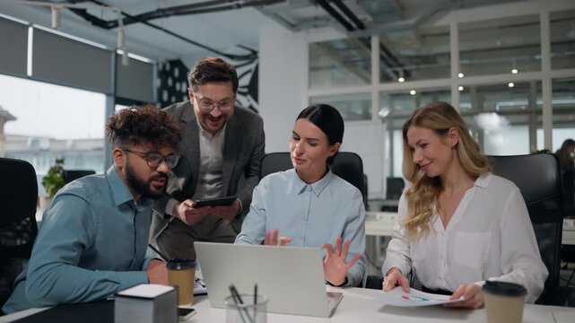 Four multiethnic business people working together with laptop talking winning job success giving high five celebrating multiracial businessmen and businesswomen colleagues win achieve team in office