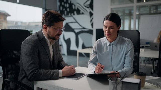 Two Caucasian business partners discuss contract papers in office businesswoman trader insurance agent bank manager woman broker talking consulting businessman client showing documents data to man