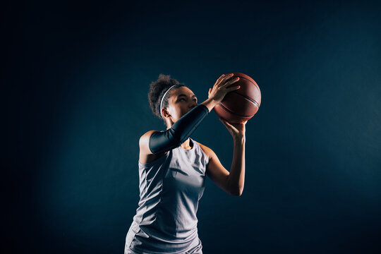 A female basketball player prepares to throw a ball against black background